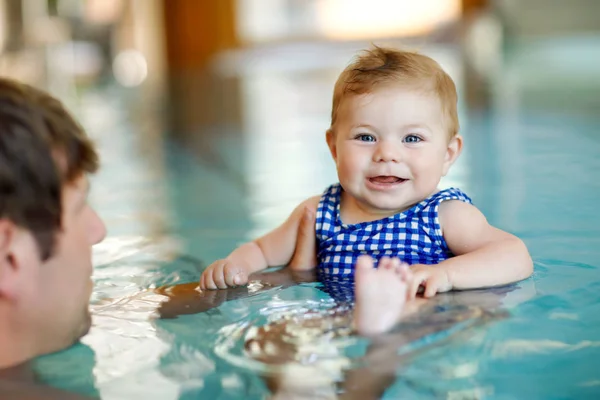 Happy middle-aged father swimming with cute adorable baby girl in swimming pool.