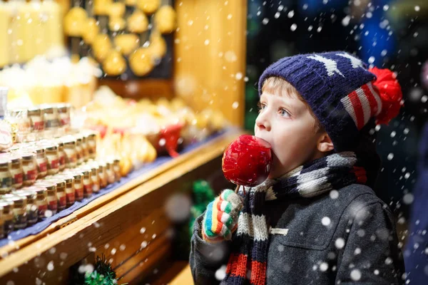 Malé dítě chlapec jí sugar apple sladkosti stojí na vánoční trh — Stock fotografie