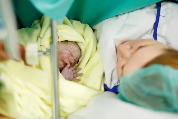 Newborn baby wrapped in blankets after birth. Mother looking for the first time on new born daughter — Stock Photo, Image
