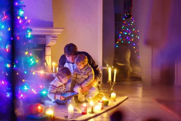 Father and his two little children sitting by fireplace chimney on Christmas Eve time.