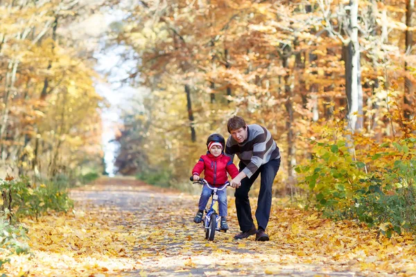 Niño y su padre en el parque de otoño con una bicicleta. Papá enseñando a su hijo a andar en bicicleta —  Fotos de Stock