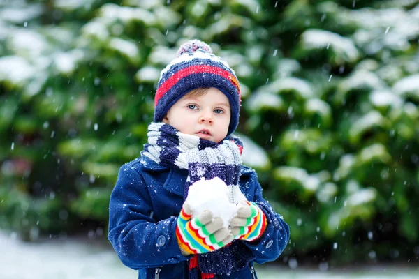 Söt liten rolig pojke i färgglada vinter mode kläder har roligt och leka med snö, utomhus under snöfall — Stockfoto