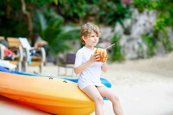 Niño bebiendo jugo de coco en la playa tropical —  Fotos de Stock