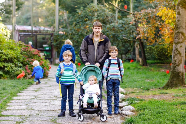 Pai feliz com três filhos caminhando pelo zoológico. Dois garotos garotos irmãos, linda menina irmã criança e pai fazendo observação de pássaros. Homem e irmãos, família saudável de quatro ao ar livre . — Fotografia de Stock