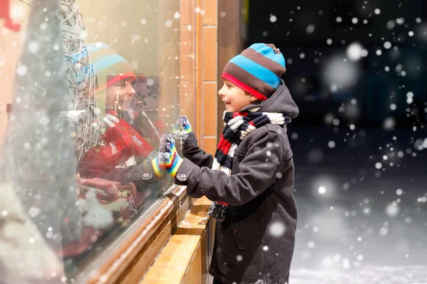 Schattige kleine school jongen jongen op de kerstmarkt. Grappige gelukkig kind in mode winterkleren waardoor venster winkelen versierd met geschenken, kerstboom. feestdagen, kerst, jeugd en mensen concept — Stockfoto