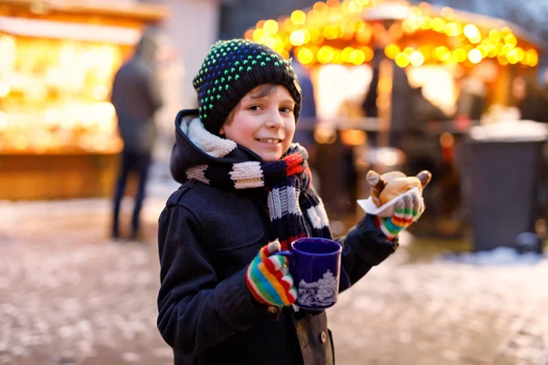 Petit garçon mignon mangeant des saucisses allemandes et buvant des enfants chauds punch sur le marché de Noël. Enfant heureux sur le marché familial traditionnel en Allemagne, Munich. Rire garçon en vêtements d'hiver colorés — Photo