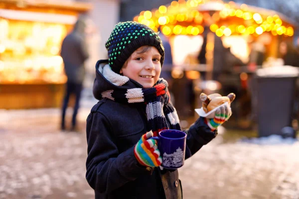 Little cute kid boy eating German sausage and drinking hot children punch on Christmas market. Happy child on traditional family market in Germany, Munich. Laughing boy in colorful winter clothes — Stock Photo, Image