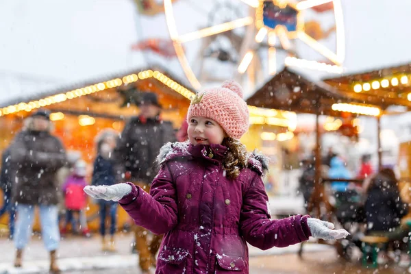 Little cute kid girl having fun on traditional German Christmas market during strong snowfall.. Happy child enjoying traditional family market in Germany, Frankfurt. Laughing girl in colorful clothes — Stock Photo, Image