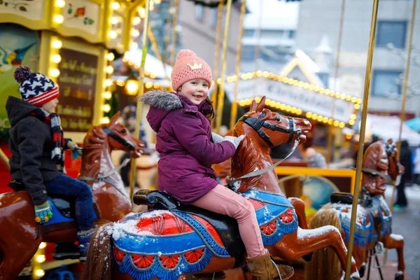 Adorable little kid girl riding on a merry go round carousel horse at Christmas funfair or market, outdoors. Happy child having fun on traditional family xmas market in Munich, Germany — Stock Photo, Image