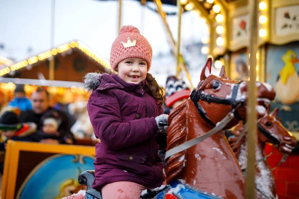 Adorabile bambina che cavalca su un allegro andare a cavallo giostra al luna park o al mercato di Natale, all'aperto. Buon bambino che si diverte sul tradizionale mercato di Natale in famiglia a Norimberga, Germania — Foto Stock