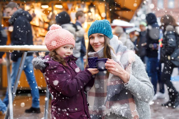 快乐的小女孩和年轻漂亮的女人，一杯热腾腾的巧克力和含酒精的葡萄酒。可爱的孩子和美丽的妈妈在德国的圣诞市场上。在圣诞市场上散步的家人. — 图库照片