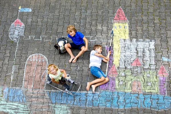 Dvě malé děti, chlapci a roztomilé batole dívka kreslení rytíř hrad s barevné křídy na asfaltu. Happy sourozenci a přátelé baví s vytvářením křídy obrazu a — Stock fotografie