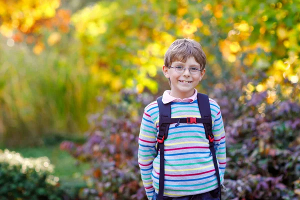 Menino feliz com óculos e mochila ou mochila em seu primeiro dia de escola no dia ensolarado do outono. Criança ao ar livre com árvores de bordo amarelas e lidas no fundo, conceito Back to school — Fotografia de Stock