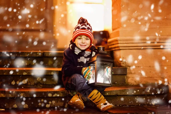 Malý roztomilý chlapeček s lucernou na schodech poblíž kostela. Happy dítě na vánočním trhu v Německu. Dítě čeká na rodiče v chladný zimní den — Stock fotografie