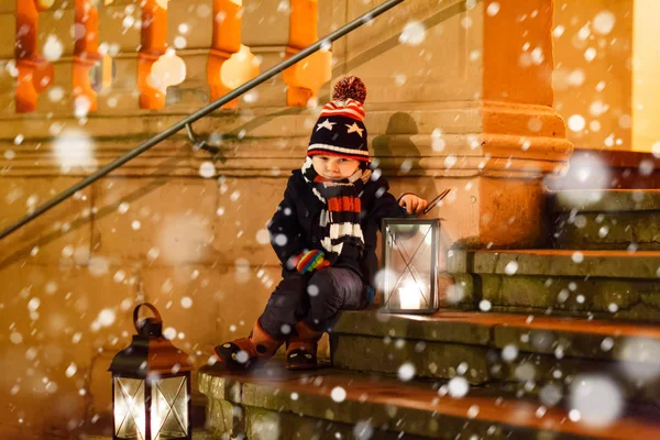 Pequeno menino bonito com uma lanterna de luz nas escadas perto da igreja. Criança feliz no mercado de Natal na Alemanha. Criança à espera dos pais no dia frio de inverno — Fotografia de Stock