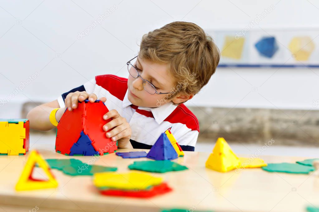 Little kid boy with glasses playing with lolorful plastic elements kit in school or preschool nursery. Happy child building and creating geometric figures, learning mathematics and geometry.