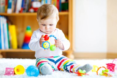 Bebek odasında eğitici oyuncaklarla oynayan sevimli bir kız. Mutlu sağlıklı çocuk evde renkli farklı oyuncaklarla eğleniyor. Bebek gelişimi ve ilk adımlar, çalmayı ve yakalamayı öğrenmek..