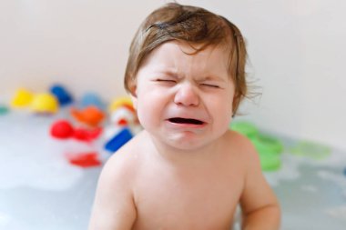Köpüklü banyo küvet içinde alarak şirin hüzünlü bebek kız. Banyo kauçuk oyuncaklar ile oynama yürümeye başlayan çocuk ağlıyor