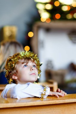 Güzel bir çocuk çocuk Noel hikaye bir kilisede bir melek oynarken. Işıkları ve xmas ağacı arka plan üzerinde mutlu sevimli sarışın çocuk. Xmas gecesi, büyük Hıristiyan, Katolik tatil kutlamaları.