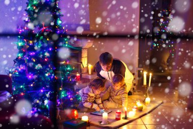Baba ve Noel arifesi zamanında şömine baca tarafından oturan iki küçük çocuğu.