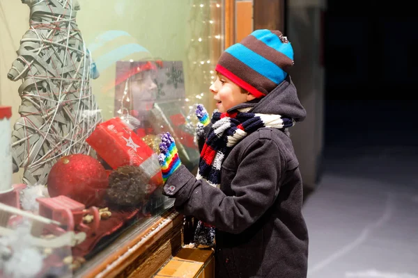 Bambino divertente felice in abiti invernali di moda facendo vetrina decorata con regali, albero di Natale — Foto Stock