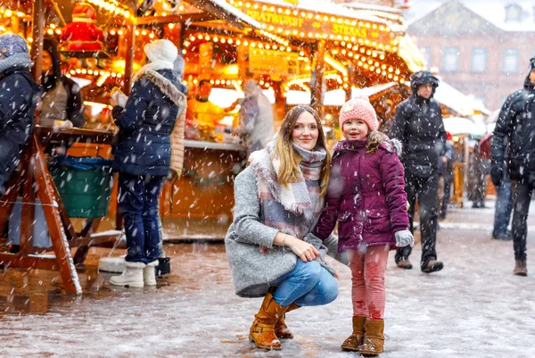 Little cute kid girl and young mother having fun on traditional German Christmas market during strong snowfall. — Stock Photo, Image