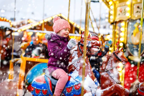 Adorable little kid girl riding on a carousel horse at Christmas funfair or market, outdoors. — Stock Photo, Image