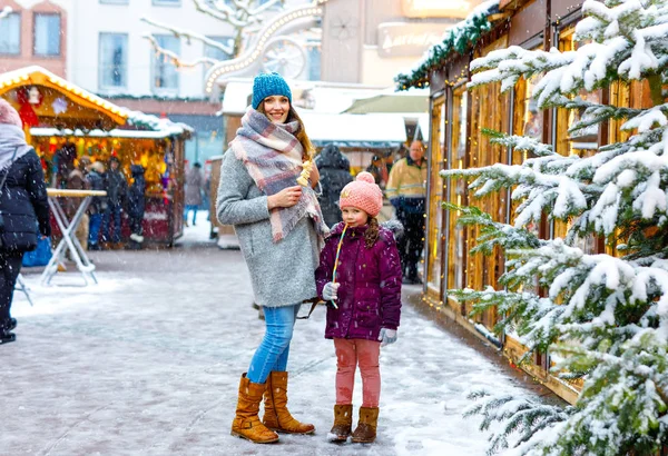 Malé roztomilé dítě dívka a mladá matka baví na tradiční německý vánoční trh během silné sněžení. — Stock fotografie