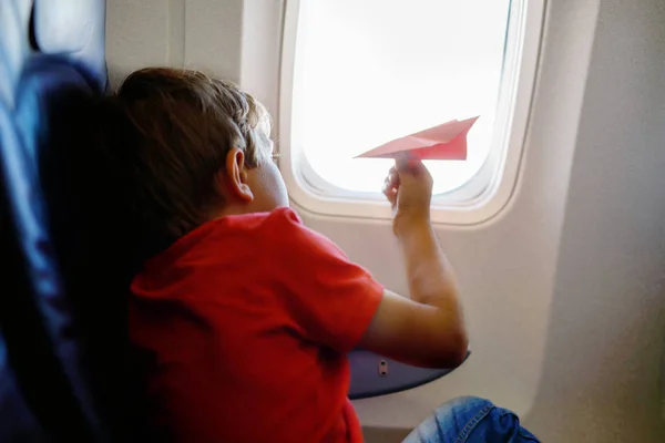 Kleine jongen jongen spelen met rood papier vliegtuig tijdens de vlucht op vliegtuig — Stockfoto