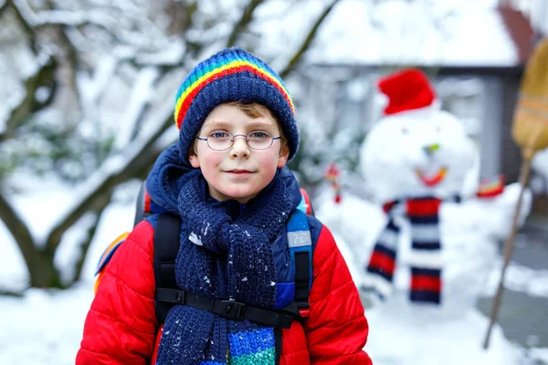 Glücklicher Junge mit Brille hat Spaß mit Schnee auf dem Schulweg, Grundschulklasse — Stockfoto