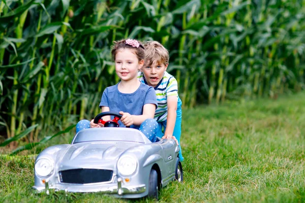 Dos niños felices jugando con un gran coche de juguete viejo en el jardín de verano, al aire libre —  Fotos de Stock