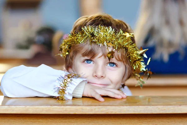 Menino bonito jogando um anjo na história de Natal em uma igreja. Criança loira adorável feliz com luzes e árvore de xmas no fundo. Celebração da véspera de Natal, grande feriado cristão, católico . — Fotografia de Stock