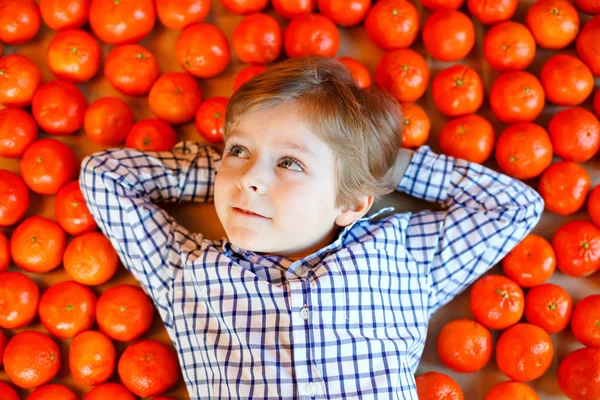 Schattige kleine jongen jongen met mandarijn sinaasappelen achtergrond. Gelukkig lachend kind plezier maken met veel fruit. Gezond eten, eten en levensstijl concept — Stockfoto