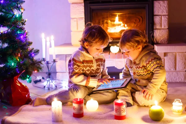 Zwei niedliche Kleinkinder, blonde Zwillinge, die mit einem neuen Tablet-Geschenk spielen. Familie feiert Weihnachtsfest — Stockfoto