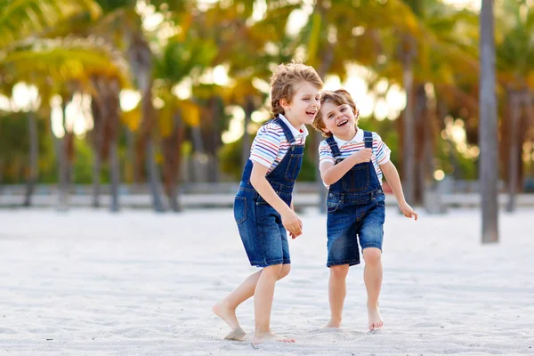 Due bambini piccoli ragazzi che si divertono sulla spiaggia tropicale, felici migliori amici che giocano, concetto di amicizia. Fratelli fratelli, gemelli in famiglia guardano con palme alberi su sfondo. Vacanze in famiglia. — Foto Stock