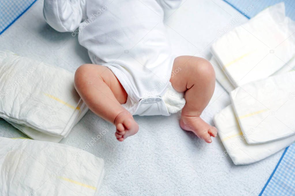 Feet of newborn baby on changing table with diapers. Cute little girl or boy two weeks old. Dry and healthy body and skin concept. Baby nursery.