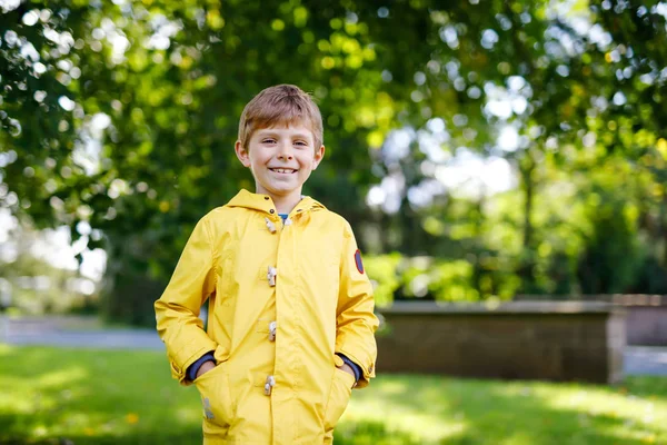 Πορτρέτο του όμορφη χαμογελαστό αγόρι παιδί. Ευτυχισμένο παιδί φόντο πράσινο δέντρο. Παιδί που παίζει σε εξωτερικούς χώρους. Υγιείς αγόρι που γελά στο κίτρινο βροχή παλτό — Φωτογραφία Αρχείου