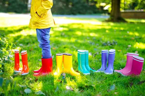 Παιδάκι με πολύχρωμο βροχή μπότες. Μεγέθυνση της σχολικής ή προσχολικής ηλικίας τα πόδια παιδί αγόρι ή κορίτσι στο διαφορετικό λαστιχένιες μπότες, τζιν και μπουφάν. Υποδήματα για το βροχερό φθινόπωρο — Φωτογραφία Αρχείου