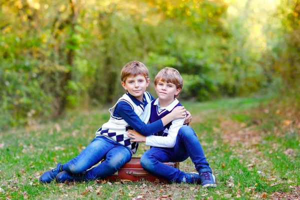 Kis iskola portréja gyerekek fiú ül az erdőben. Boldog gyermekek, legjobb barátok, és birtoklás móka a meleg napsütéses napon kora ősszel testvérek. Ikrek és a család, a természet és aktív pihenés. — Stock Fotó