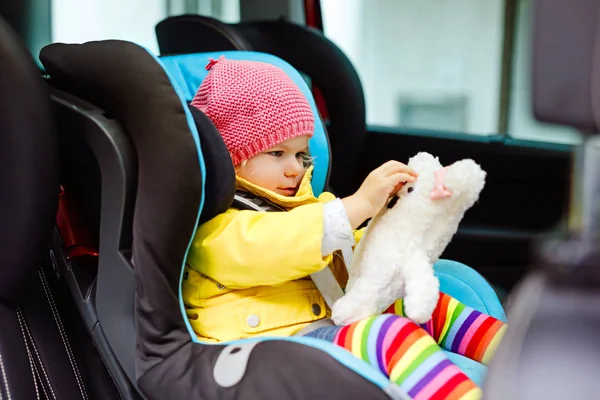 Adorable baby girl with blue eyes and in colorful clothes sitting in car seat. Toddler child in winter clothes going on family vacations and jorney. Safe travel, children safety, transportation — Stock Photo, Image