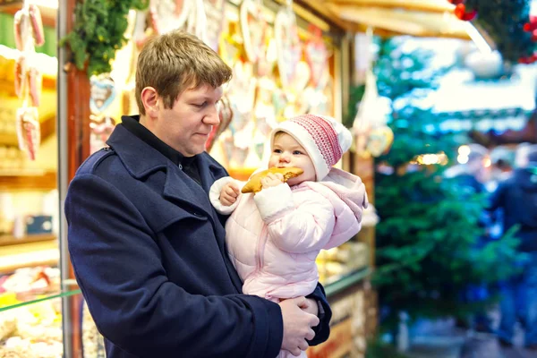 Padre de mediana edad sosteniendo bebé hija niña cerca de soporte dulce con pan de jengibre y nueces . — Foto de Stock
