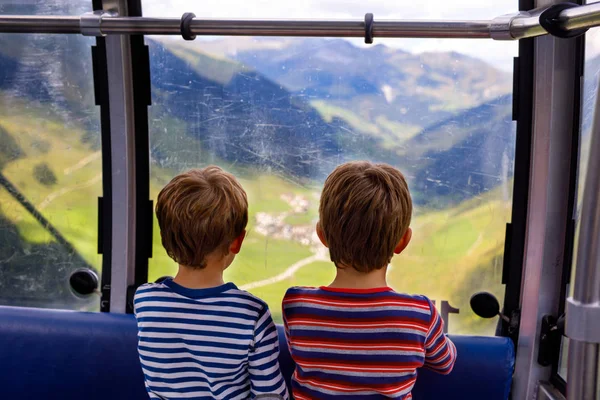 Двоє маленьких хлопчиків сидять всередині кабіни кабельного автомобіля і дивляться на гірський пейзаж . — стокове фото