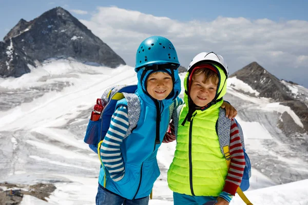 Två små pojkar med Skyddshjälmar och kläder med berg landskap bakgrunder. Barn vandra och upptäcka glaciären i Tirol, Österrike, Hintertux — Stockfoto