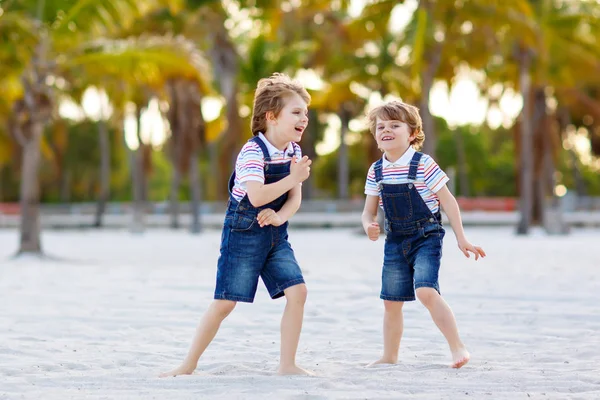 Dwoje małych chłopców bawiących się na tropikalnej plaży, szczęśliwi przyjaciele grający, koncepcja przyjaźni. Bracia rodzeństwo, bliźnięta w rodzinie wyglądają z palmami na tle. Wakacje rodzinne. — Zdjęcie stockowe