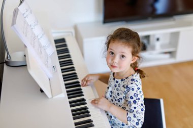 Oturma odasında ya da müzik okulunda piyano çalan güzel bir kız çocuğu. Anaokulu çocuğu müzik aleti çalmayı öğrenirken eğleniyor. Eğitim, beceri kavramı