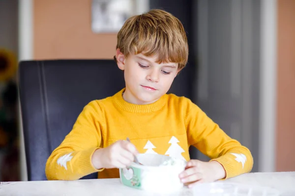 Niño rubio con pelos rizados comiendo helado en casa o en el jardín de infantes. Hermoso niño con gran caja de helado — Foto de Stock