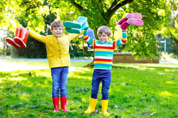 Zwei kleine Jungen, süße Geschwister mit vielen bunten Regenstiefeln. Kinder in verschiedenen Gummistiefeln und Jacken. Schuhe für den verregneten Herbst. Gesunde Zwillinge und beste Freunde haben Spaß im Freien — Stockfoto