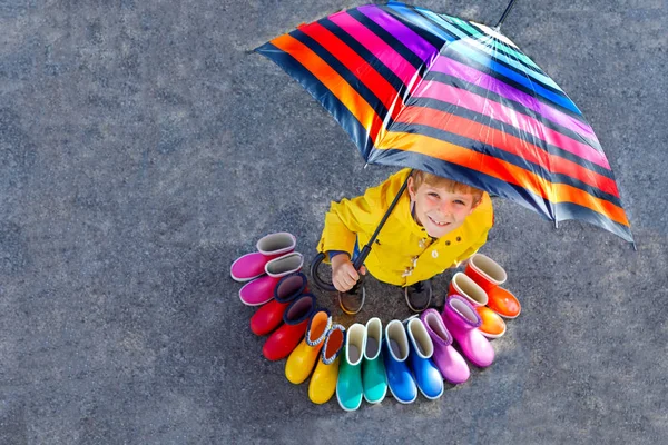 Kleiner Junge und eine Gruppe bunter Regenstiefel. blondes Kind, das unter Regenschirm steht. Nahaufnahme von Schulkindern und verschiedenen Gummistiefeln aus hohem Winkel. Schuhe für den verregneten Herbst — Stockfoto