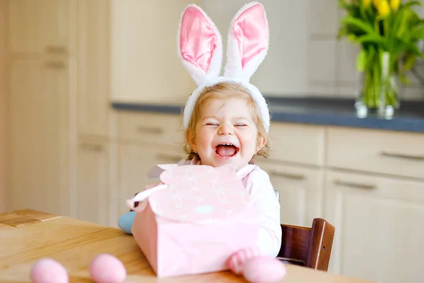 Roztomilé malé batole dívka na sobě velikonoční zajíček uši hrát s barevnými pastelovými vejci. Šťastné dítě vybaluje dárky. Rozkošné zdravé usměvavé dítě v růžových šatech těší rodinnou dovolenou — Stock fotografie