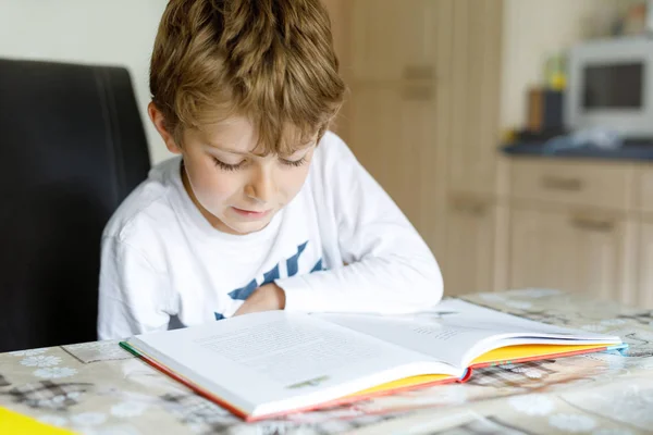 Un ragazzino biondo che legge un libro a casa. Bambino interessato a leggere la rivista per bambini. Tempo libero per i bambini, costruzione di competenze e concetto di istruzione — Foto Stock